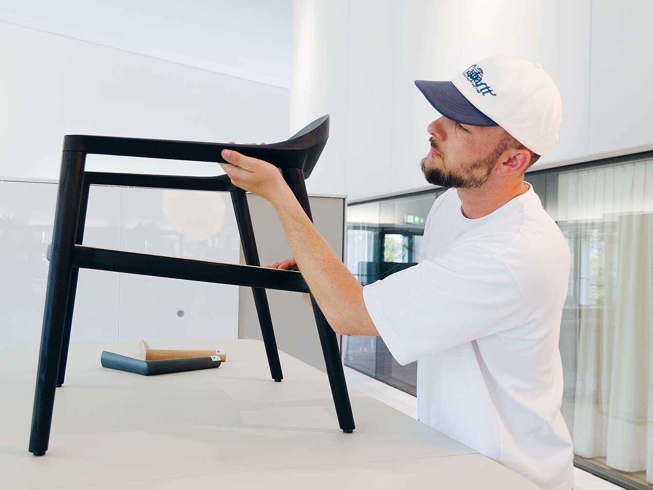 El diseñador Konstantin Thomas examina la silla se:café de madera negra, destacando su artesanía duradera y cómoda.