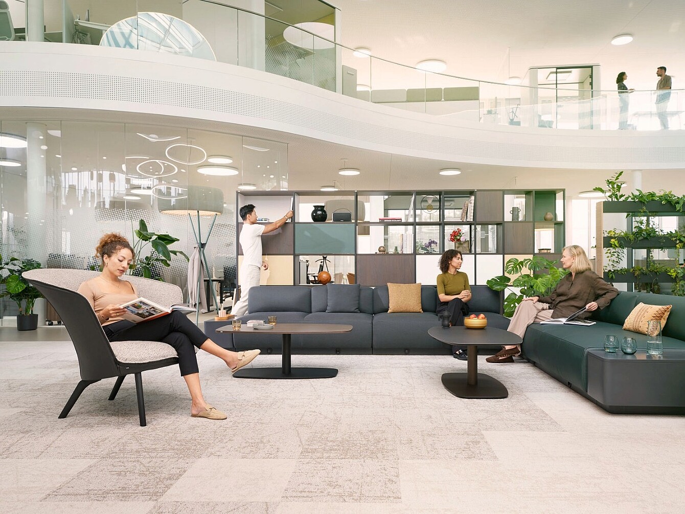 Modern open library zone with seating groups, shelves, and people reading, conversing, and using a whiteboard.