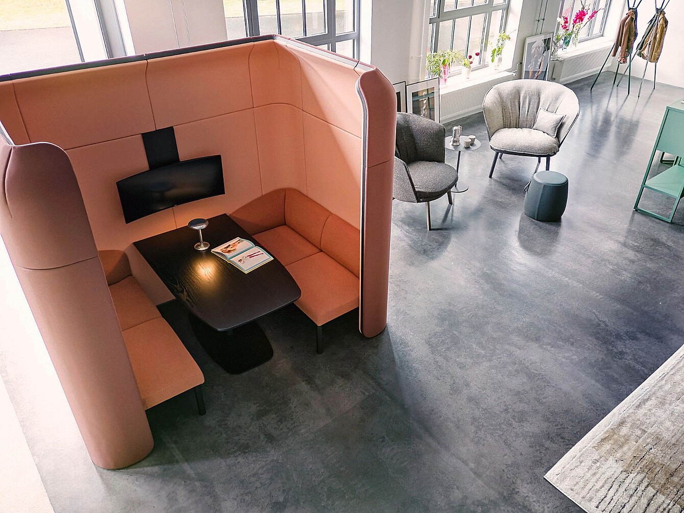 Modular se:hive seating pod con paredes altas y banco integrado alrededor de una mesa negra, junto a dos sillones y una pequeña mesa redonda en un espacio de oficina luminoso con grandes ventanas.