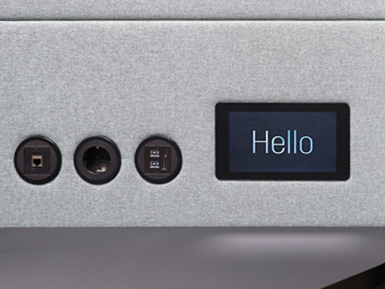 Primo piano del pannello di un dispositivo che mostra tre porte circolari e un piccolo display touch rettangolare con la parola “Ciao”.