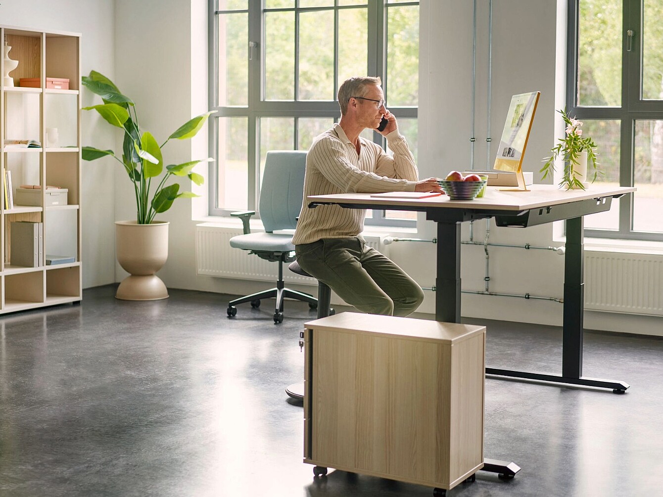 Persoon zittend op een se:fit-stoel voor een in hoogte verstelbaar bureau in een licht kantoor met grote ramen en planten