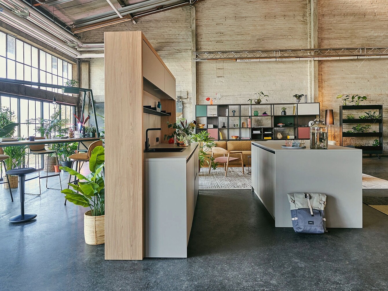 Interni moderni del se:café bar, un’isola centrale, scaffali aperti con piante e decorazioni e grandi finestre in stile industriale