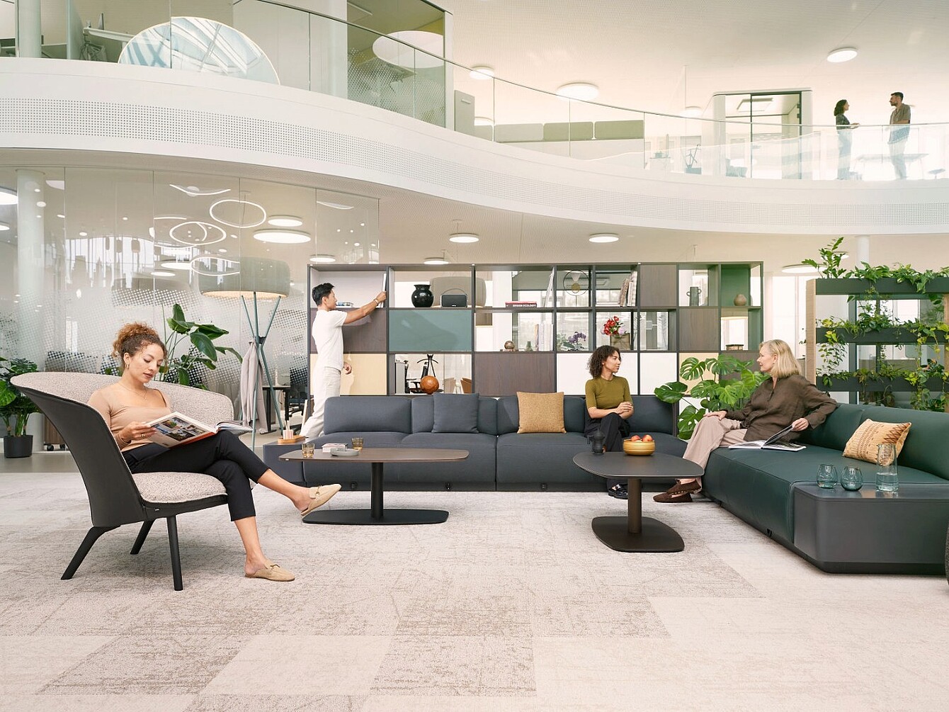 Area lounge moderna con divani modulari, poltrone, tavolini bassi, scaffali e persone impegnate in conversazioni e attività