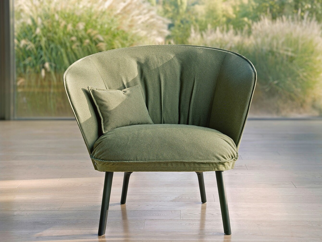 Poltrona se:living verde con cuscino abbinato su un pavimento in legno con piante sfocate sullo sfondo