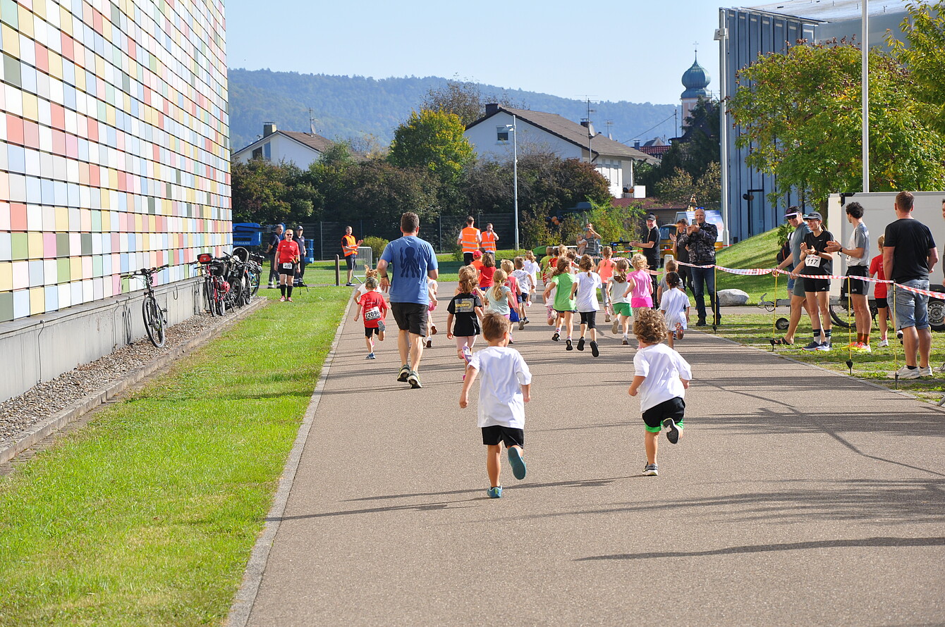 Kinder laufen beim Sedus RUN 2025 auf einem asphaltierten Weg, begleitet von Erwachsenen und Zuschauern bei sonnigem Wetter.