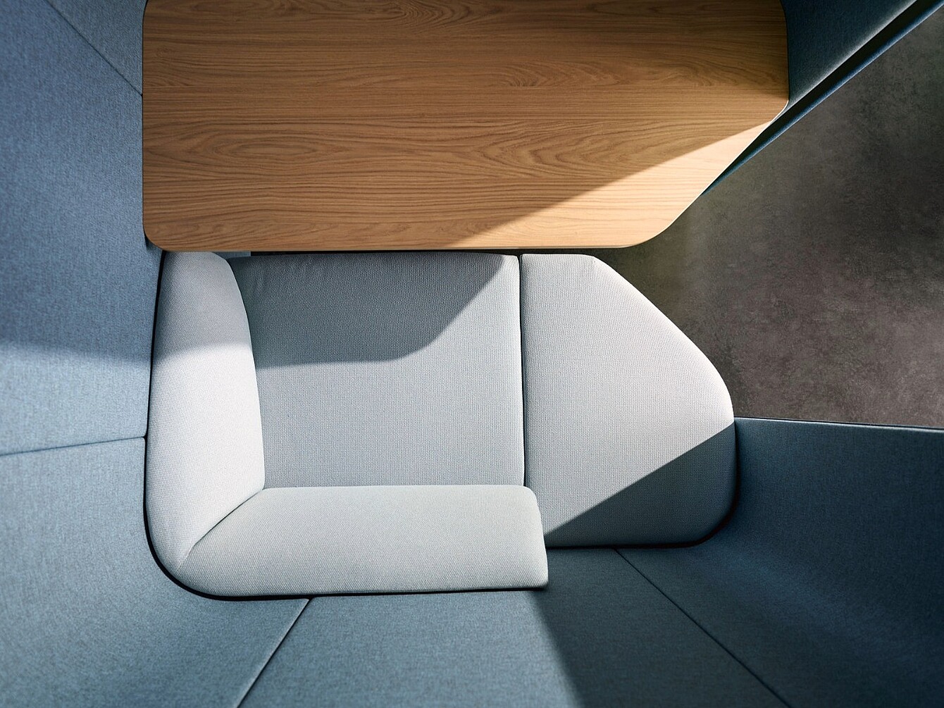 Vista superior de una unidad de asientos modular con cojines gris claro y una superficie de mesa de madera en un espacio esquinero.