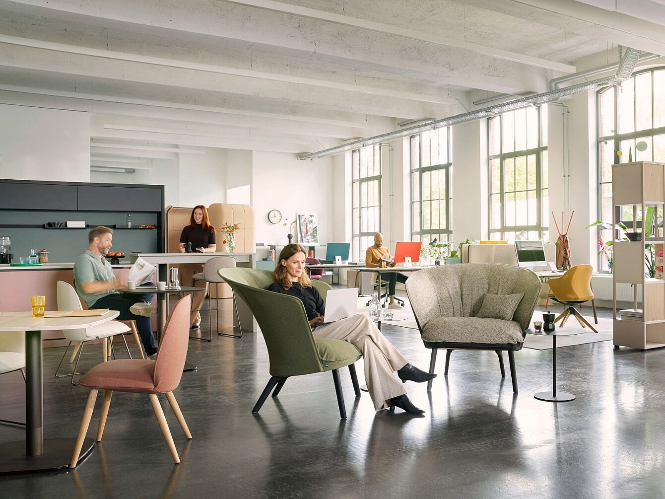Open-plan office with large windows and multiple people working at desks and sitting in armchairs, featuring modern furniture and a spacious layout