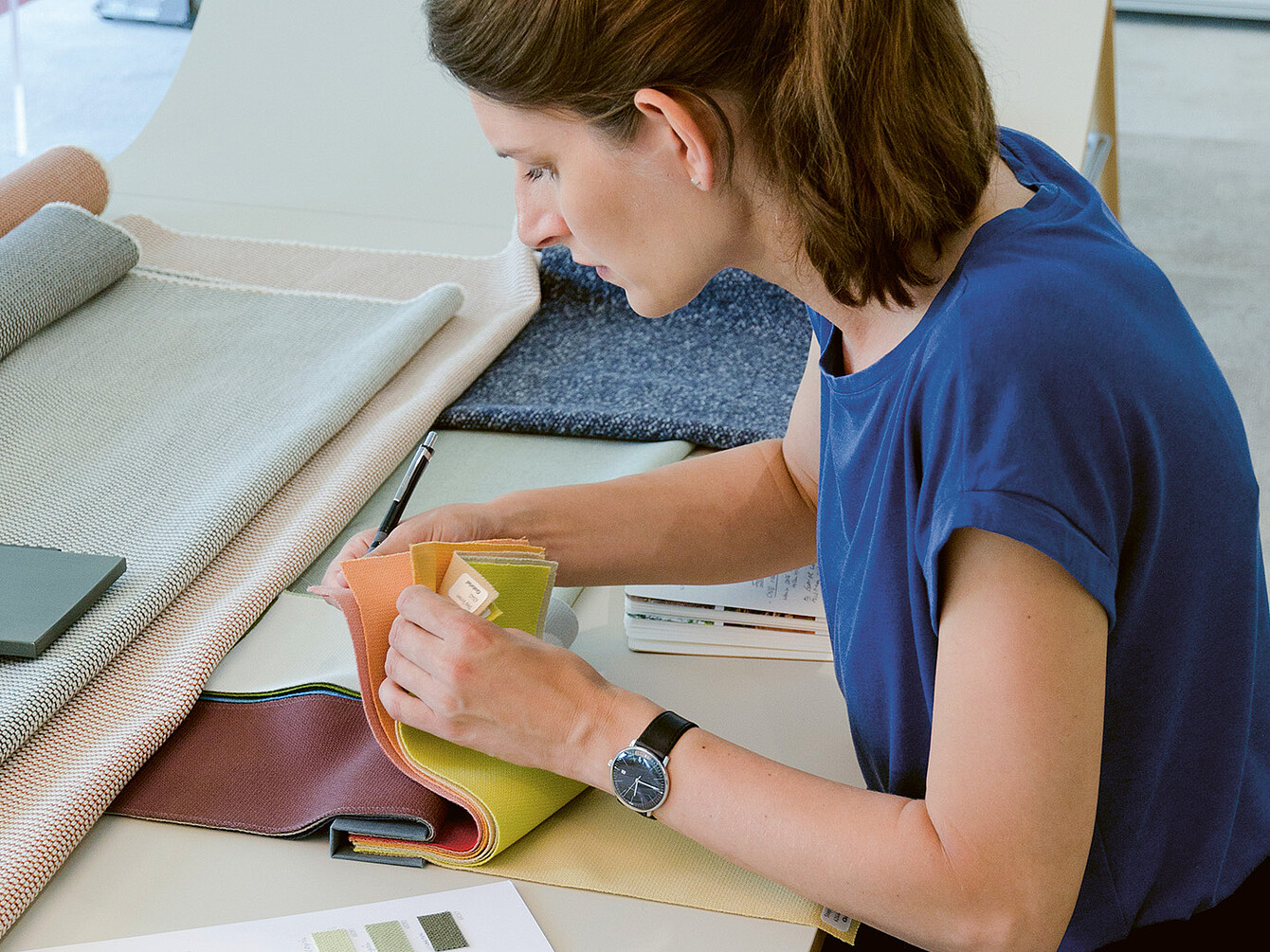 La diseñadora industrial Judith Daur examina muestras de tela, centrándose en el color y la textura, en un espacio de trabajo lleno de materiales diversos. 