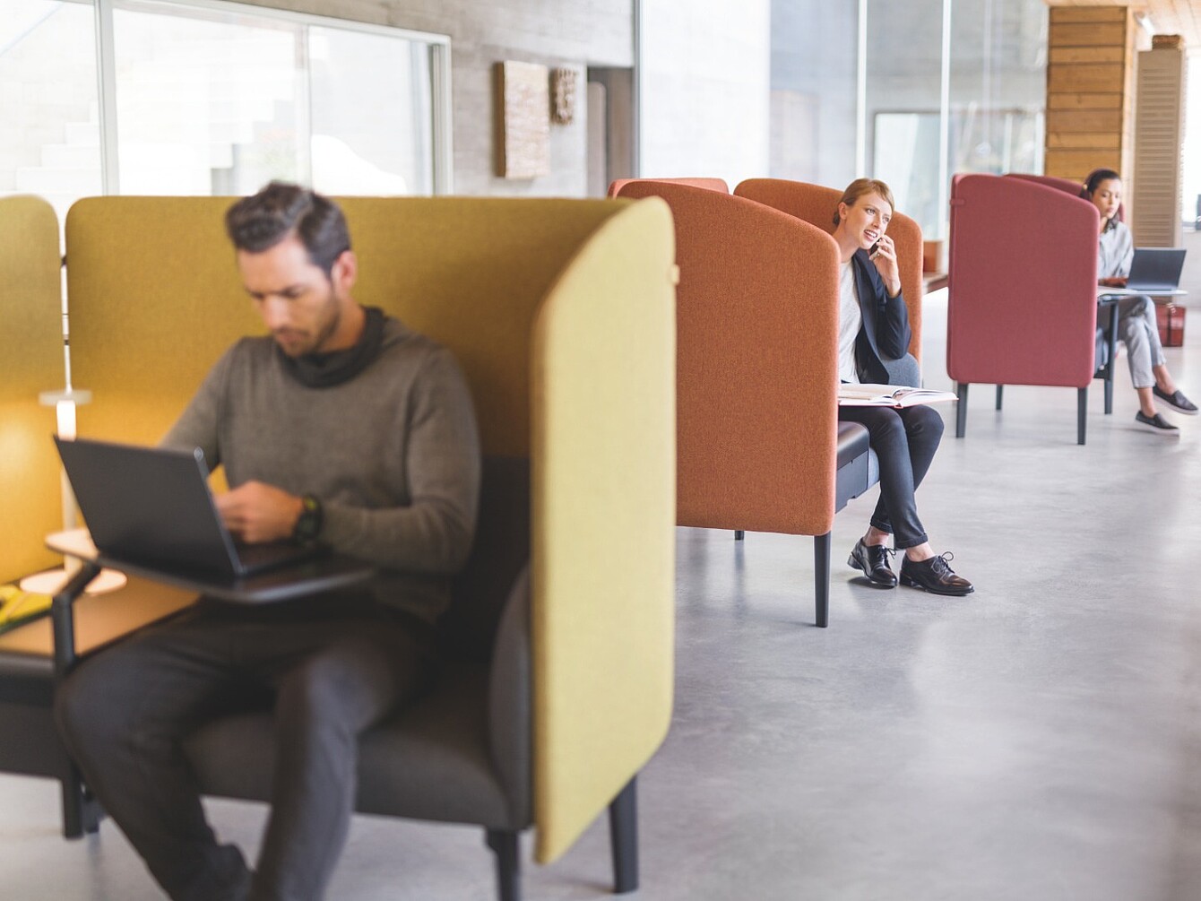 Two people sit separately in differently colored booth seats in a modern open space