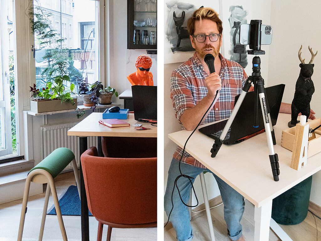 Person sitting at a white table with a laptop and microphone, in front of a smartphone on a tripod, with artworks and plants in the background.