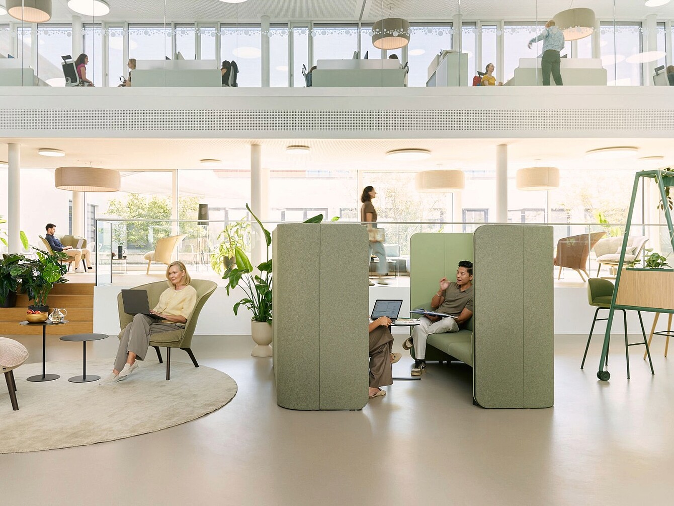Espacio de oficina abierto con se:hive modular que crea áreas de retiro semicerradas, rodeadas de sillas, mesas, plantas y personas trabajando o caminando.
