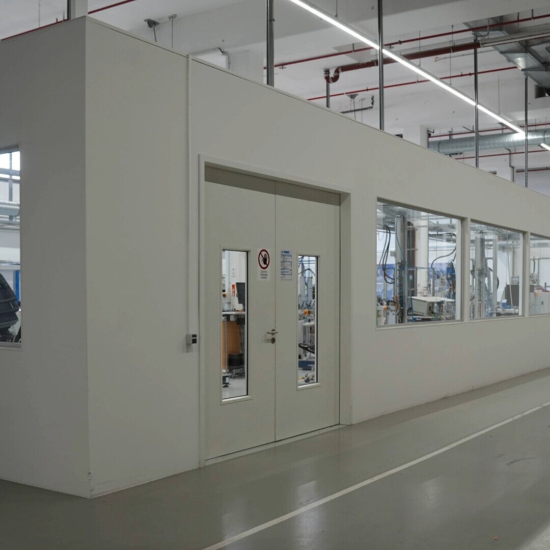 Long white rectangular test laboratory room with multiple windows and a glass door inside a large industrial space