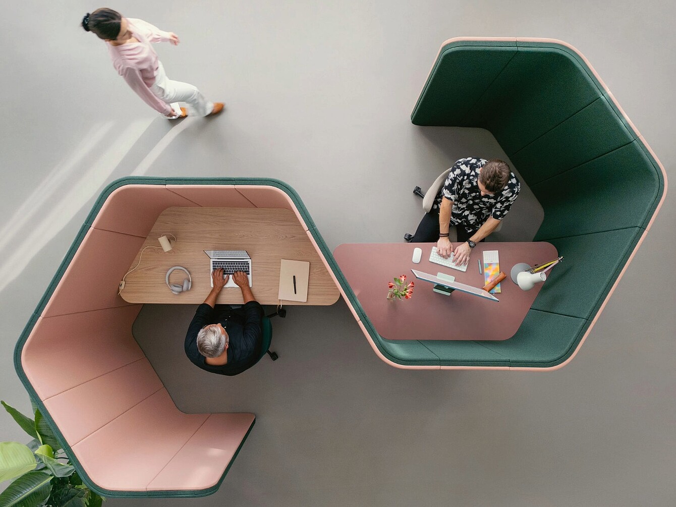 Dos puestos de trabajo hexagonales se:hive con paredes tapizadas altas, uno con una persona utilizando un ordenador portátil y auriculares, y otro con una persona trabajando en un ordenador de sobremesa, vistos desde arriba.
