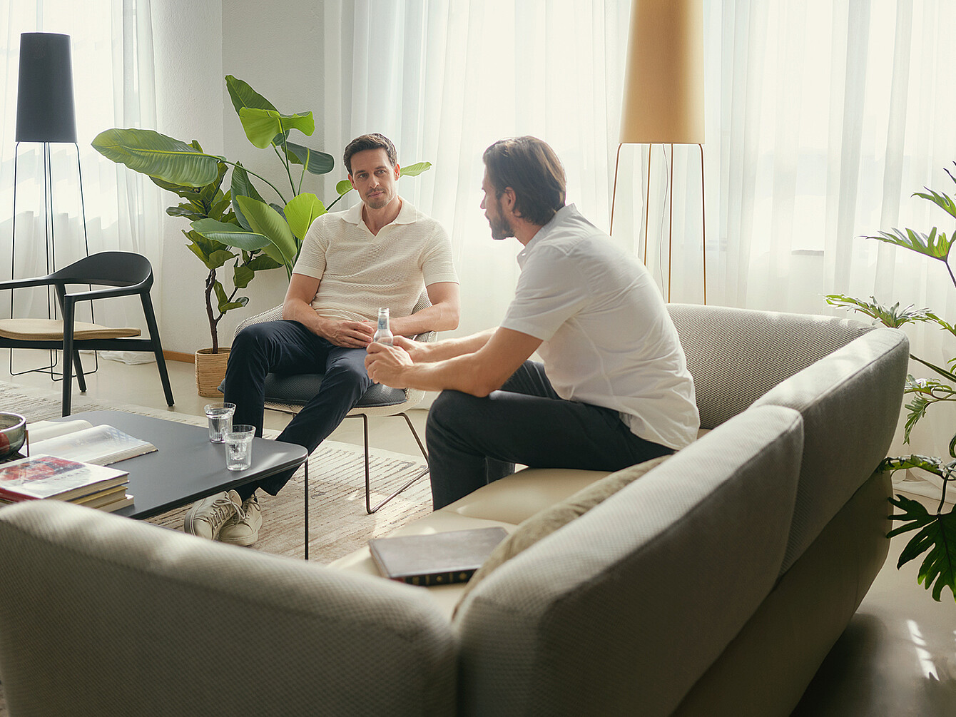 Dos hombres mantienen una conversación en un luminoso salón de oficina con mobiliario moderno y plantas, que ilustra la interacción intencionada en la oficina.