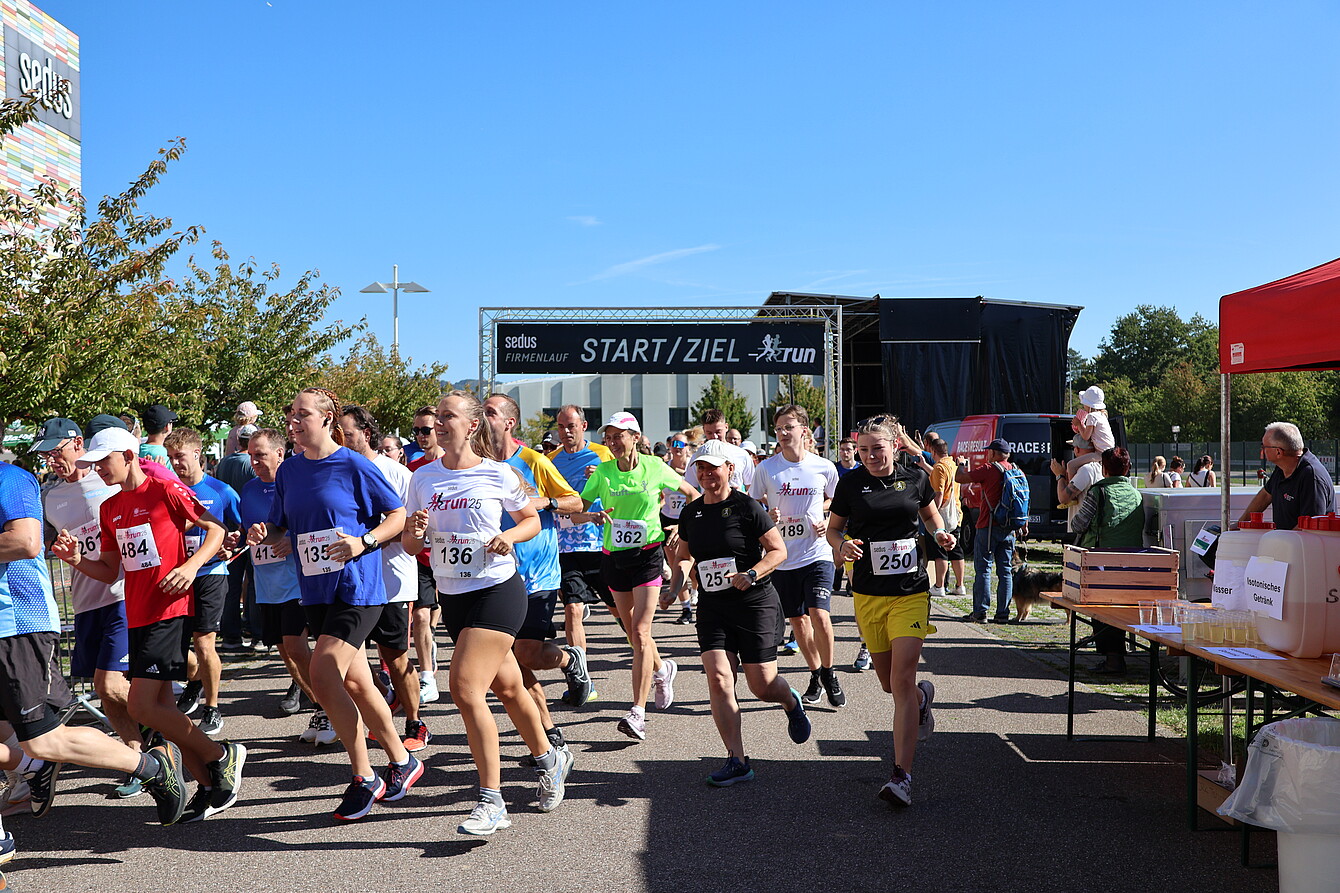 Mehrere Läufer starten beim Sedus RUN 2025 unter dem Banner 'START/ZIEL' bei sonnigem Wetter, tragen Laufnummern und Sportkleidung.