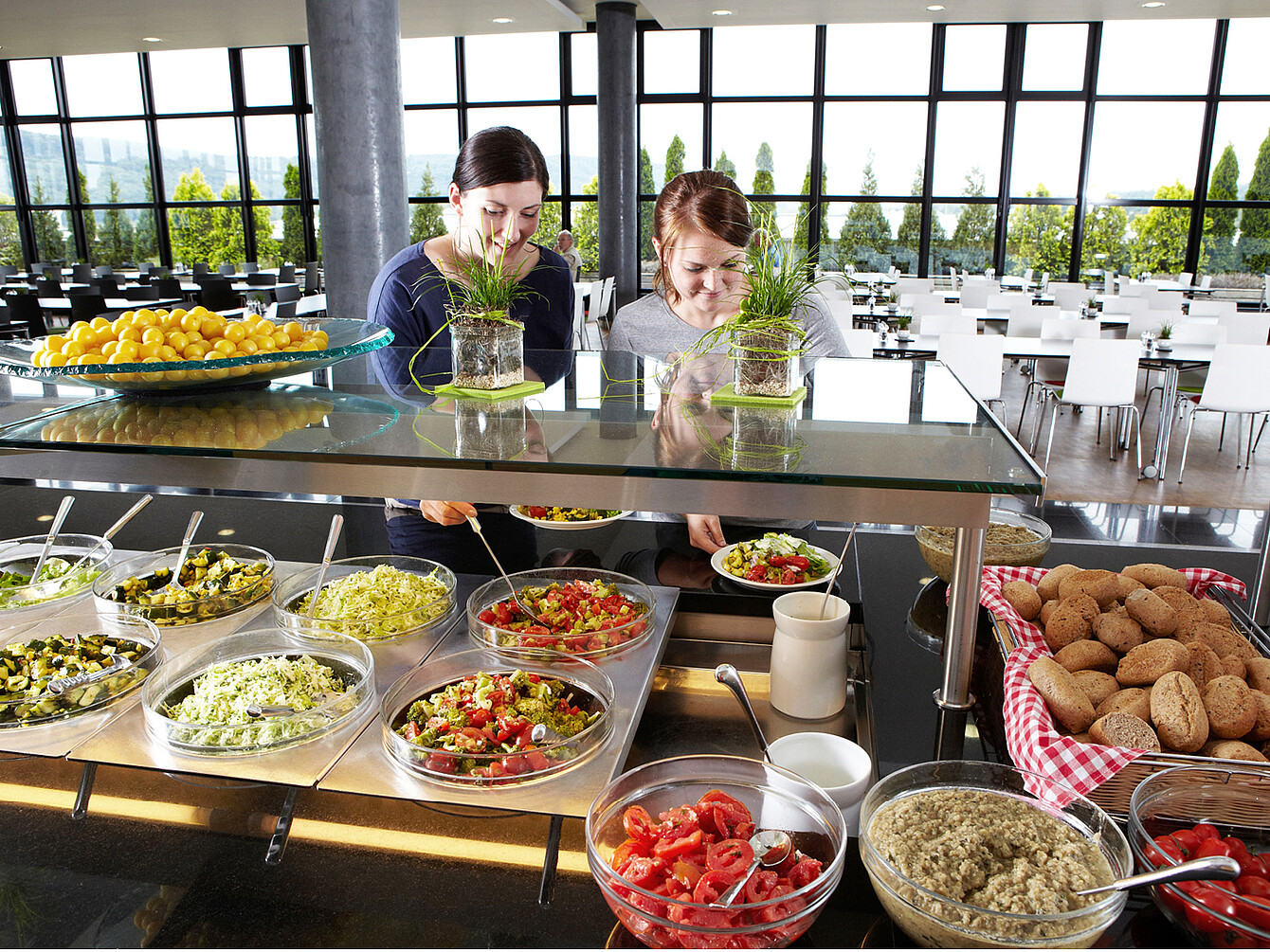 Due donne scelgono insalate fresche e opzioni alimentari salutari in un buffet di catering sostenibile in una caffetteria moderna e luminosa sul posto di lavoro