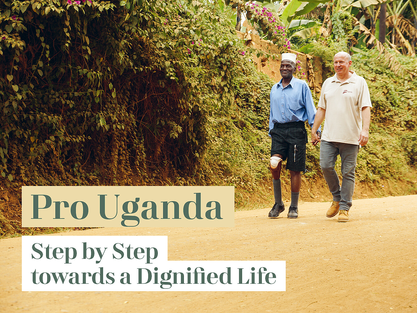 Dos hombres caminando por un sendero de tierra junto a un denso seto verde, uno con camisa azul y pantalones cortos negros con una prótesis en la pierna, el otro con polo beige y vaqueros, cogidos de la mano. El texto dice «Pro Uganda» y «Paso a paso hacia una vida digna».