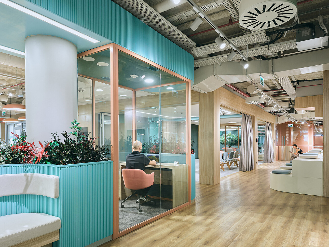 Interior de la oficina diáfana en la sede de Ford Otosan en Izmit, con sala de reuniones con paredes de cristal, suelo de madera, zonas de descanso y conductos de techo visibles