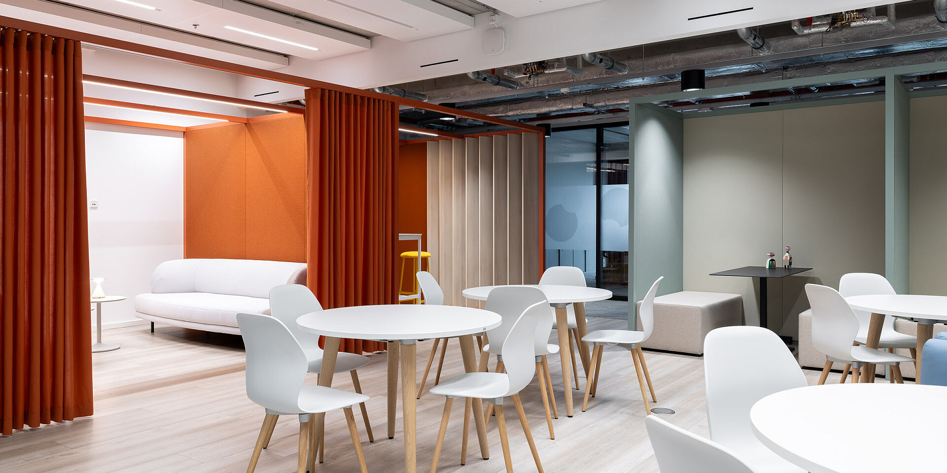 Modern bistro area at Veolia with white se:spot designer chairs and se:assist tables, orange wall and white couch in the background  