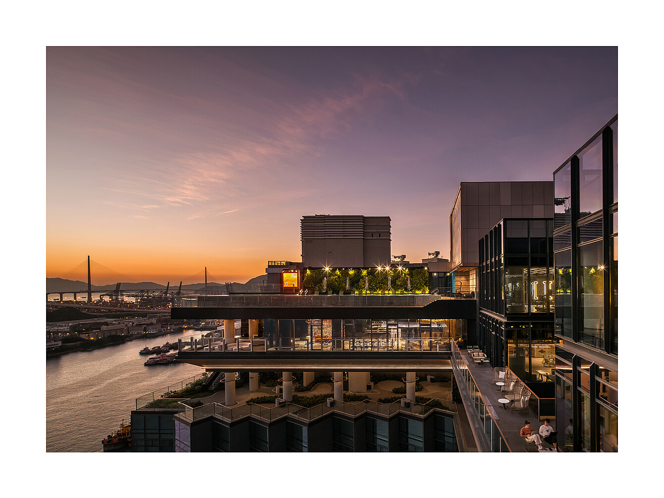Immeuble moderne de plusieurs étages avec terrasses et murs en verre donnant sur une rivière au coucher du soleil 