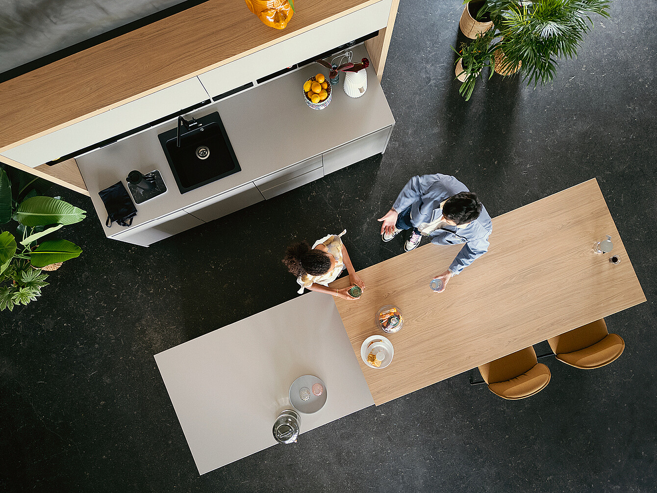 Vista dall'alto di due persone che conversano a un tavolo in legno in uno spazio di lavoro ibrido e flessibile con zona cucina integrata e piante